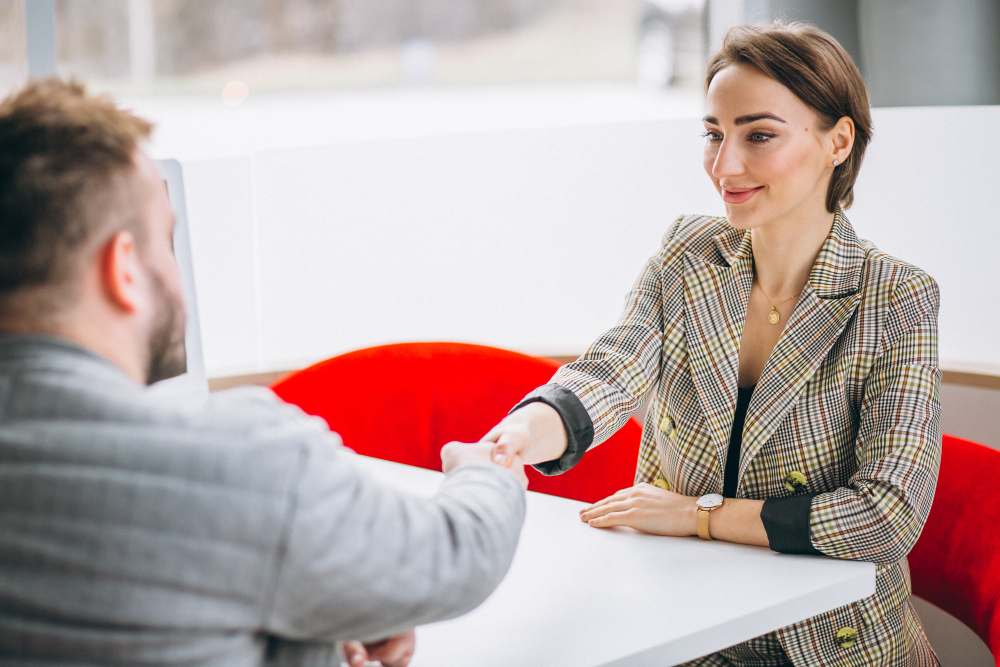 A woman in a business suit shakes hands with a man, symbolizing professional collaboration in a personalized escort referral service.