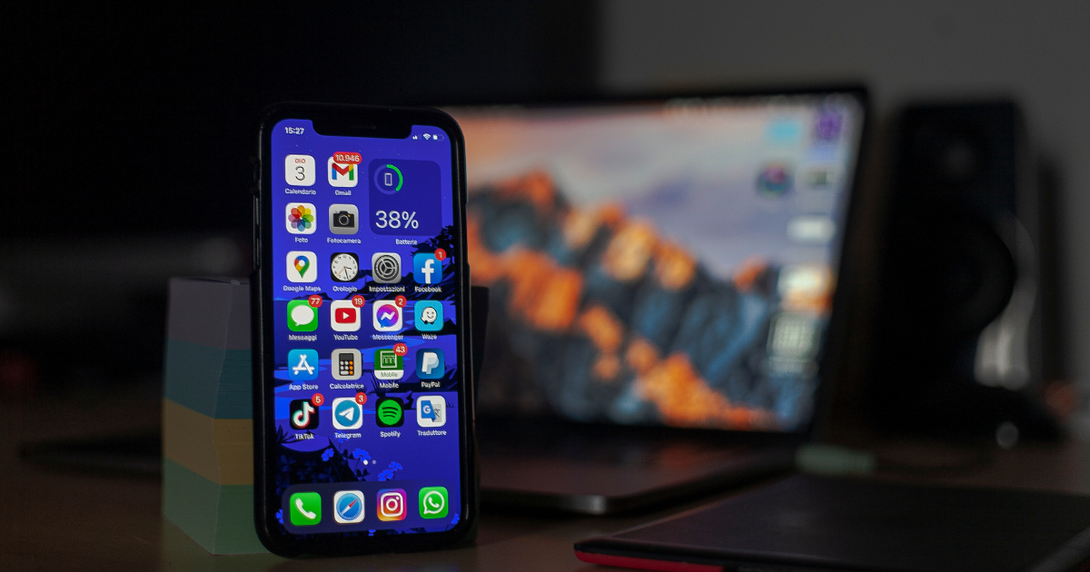 Smartphone displaying various app icons with a blurred laptop in the background, representing modern app solutions and mobile technology.