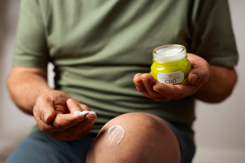 A man with a jar of Max Relief Recovery Gel by Zentric Life on his knee, intended for pain and muscle relief.
