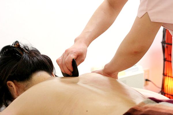 Therapist performing a traditional gua sha back massage using a smooth stone tool.